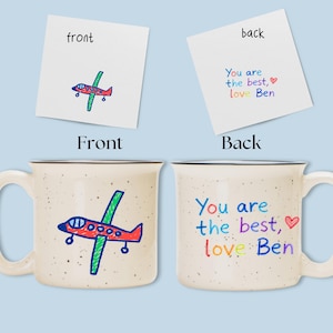 May include: A speckled ceramic mug with a black rim, featuring a hand-drawn airplane on the front and the text "You are the best, love Ben" on the back. The airplane is red, green, and blue.