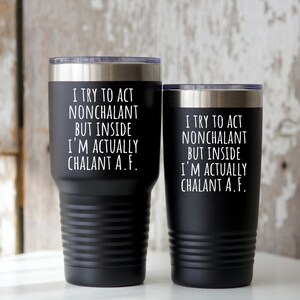 May include: Two black insulated tumblers with silver rims and lids. The tumblers have the text "I TRY TO ACT NONCHALANT BUT INSIDE I'M ACTUALLY CHALANT A.F." in white lettering. The tumblers are cylindrical with a textured design.