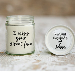 May include: A white candle in a glass jar with the text "I miss your sweet face" on the label. The lid of the jar is white with the text "Visiting October 8 ♥ Jenna".