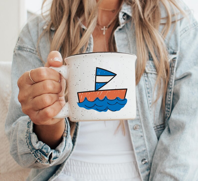May include: White ceramic mug with a black rim and a sailboat illustration. The sailboat features a blue and white sail, an orange hull, and blue waves. The mug has a speckled design.