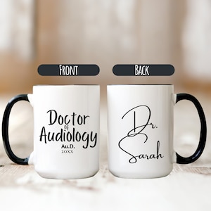 May include: White coffee mug with a black handle and black rim. The front of the mug says "Doctor of Audiology Au.D. 20XX". The back of the mug says "Dr. Sarah" in cursive.