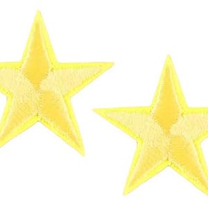 May include: Two yellow star-shaped embroidered patches. Each star has a bright yellow outline and a lighter yellow centre. The patches are likely for decorative purposes, such as adorning clothing or accessories.