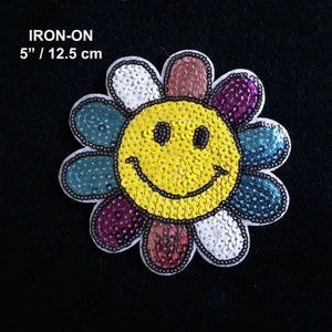 May include: A sequined iron-on patch shaped like a smiling flower. The face is yellow, and the petals are various colors. The patch is 12.5 cm in diameter, with the text "IRON-ON" above. A fun, decorative item.