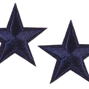May include: Two navy blue embroidered star patches. Each star has five points and a textured appearance. These patches could be used for decorative purposes on clothing or accessories.
