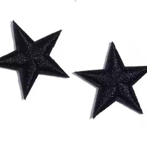 May include: Two black star-shaped patches with a textured finish, set against a white backdrop. These patches are suitable for clothing embellishment or craft applications.