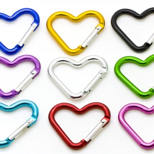 May include: Nine heart-shaped carabiner clips in various colours: blue, gold, black, purple, silver, green, red, teal, and pink. Each clip has a silver spring-loaded gate for secure attachment. These decorative clips are ideal for keychains or accessories.