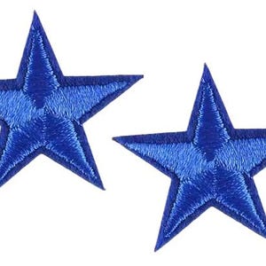 May include: Two embroidered blue star patches. Each star features a five-point design with a lighter blue centre and a darker blue outline. These patches are likely for decorative use.