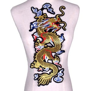 May include: Embroidered patch depicting a golden dragon with red, blue, and white details. The dragon is set against a backdrop of stylized clouds with black and blue borders. The patch is designed for sewing onto fabric.
