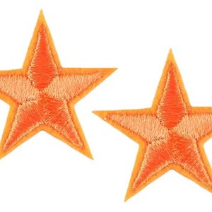 May include: Two embroidered star patches. Each star is orange with a lighter orange centre. The patches are five-pointed and have a stitched texture, suitable for embellishing clothing or accessories.