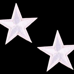 May include: Two white star-shaped embroidered patches on a black background. The stars have a five-point design with a textured, stitched appearance. These patches could be used for clothing or craft projects.