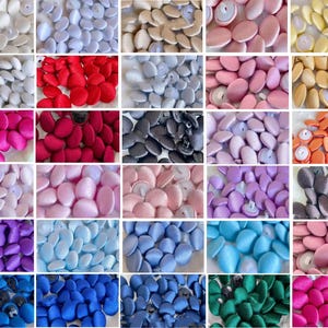 May include: A collection of round fabric-covered buttons displayed in a grid of thirty individual squares. Each square features buttons in a distinct solid colour, including shades of white, red, blue, green, yellow, pink, purple, and black.