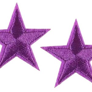 May include: Two embroidered purple star patches. Each star has five points and is filled with detailed stitching. The patches are likely for decorative purposes, such as embellishing clothing or accessories.