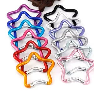 May include: A selection of star-shaped carabiner clips in a range of colours, such as blue, pink, red, and silver. These metal clips feature a spring-loaded gate for secure attachment, ideal for keychains or small items.