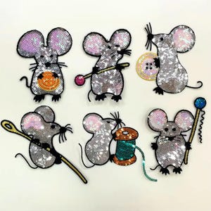 May include: Six sequined mouse patches in various poses. The mice are silver with pink and purple ears. Some mice hold sewing tools like needles, buttons, and spools of thread. One mouse has an orange belly.
