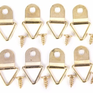 May include: Eight gold-coloured picture frame hangers with matching screws. Each hanger has a triangular loop and a rectangular top with a hole for hanging. The screws are small and gold-coloured.