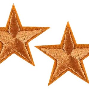 May include: Two orange embroidered star patches. Each star features a five-point design with detailed stitching, suitable for embellishing garments or accessories. The patches are displayed on a white background.
