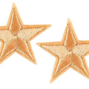 May include: Two embroidered star patches. Each patch is a five-pointed star with a light tan outline and a lighter tan fill. The patches are on a white background.