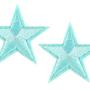 May include: Two turquoise embroidered star patches. Each patch features a five-pointed star design with a lighter turquoise centre and a darker turquoise outline. These patches are likely for decorative use.