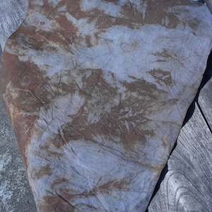 Puede incluir: Un trozo de tela con un patrón de teñido anudado azul y marrón. La tela está doblada y colocada sobre una superficie de madera.