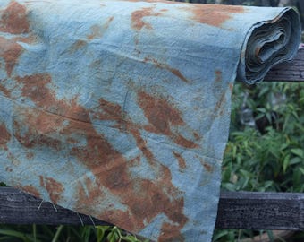 May include: A blue fabric with rust-colored dye patterns. The fabric is folded and rolled up, and is sitting on a wooden fence.