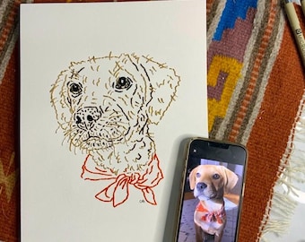 May include: A detailed pen and ink drawing of a dog with a red bow tie, next to a smartphone displaying a photo of the dog. The artwork is on a cream-colored paper, set on a colorful woven textile.