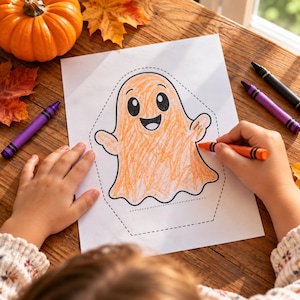 May include: A white sheet of paper featuring a black outline of a ghost, partially colored in with orange crayon. The ghost has large black eyes and a wide smiling mouth. An orange crayon is held to color the ghost, with purple and black crayons nearby.