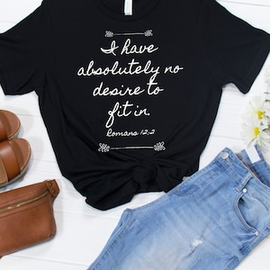 May include: Black t-shirt with white text that reads "I have absolutely no desire to fit in. Romans 12:2". The shirt is styled with a knot in the front and is paired with blue jeans and a brown leather fanny pack.