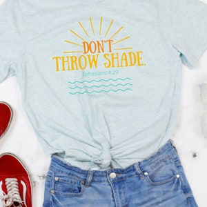 May include: A light blue t-shirt with the text "DON'T THROW SHADE. Ephesians 4:29" in orange and yellow. The shirt has a sun graphic with rays and a wavy blue line design.