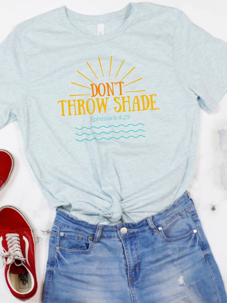 May include: A light blue t-shirt with the text "DON'T THROW SHADE. Ephesians 4:29" in orange and yellow. The shirt has a sun graphic with rays and a wavy blue line design.