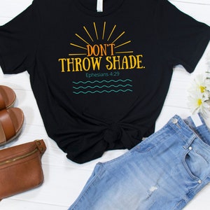May include: Black t-shirt with the text "Don't Throw Shade." in orange and yellow with a sun graphic. The text "Ephesians 4:29" is below the graphic.