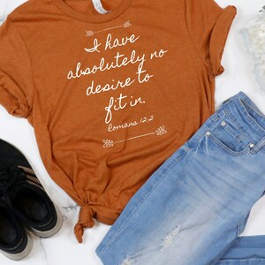 May include: A rust-coloured t-shirt with the text "I have absolutely no desire to fit in. Romans 12:2" printed in white.