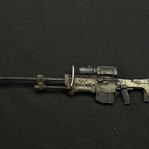 May include: A black and grey sniper rifle with a scope and a camouflage pattern. The rifle has a black barrel and a grey stock.