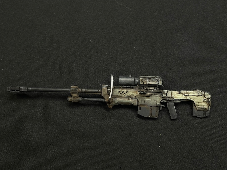 May include: A black and grey sniper rifle with a scope and a camouflage pattern. The rifle has a black barrel and a grey stock.