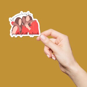 May include: A sticker featuring a graphic of three people hugging, with the text "if you wanna be my love you gotta get with my friends" in a handwritten style. The sticker has a white border and is held against a mustard-colored background.