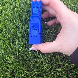 Könnte beinhalten: Ein leuchtend blaues, bewegliches Fidget-Spielzeug, bestehend aus einer Reihe verbundener, rechteckiger Segmente mit texturierten, gerillten Oberflächen und kleinen, erhabenen kreisförmigen Noppen an der Oberkante, konzipiert für taktile Manipulation.