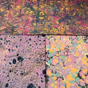 May include: Three sheets of paper featuring marbled patterns. The top sheet displays a dense swirl of pink, yellow, and dark blue. The bottom left sheet has a light pink base with dark blue spots. The bottom right sheet shows large pink, yellow, and teal circles.