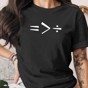 Puede incluir: Camiseta negra con un gráfico blanco de símbolos matemáticos: igual, mayor que y división. La camiseta es de cuello redondo.