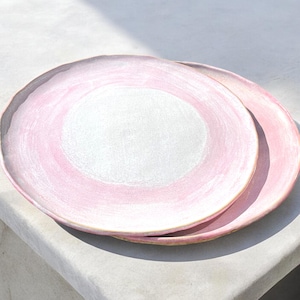 Può includere: Due piatti in ceramica rosa con un centro bianco e una sfumatura rosa. I piatti sono rotondi e hanno un bordo leggermente rialzato. I piatti sono impilati l'uno sull'altro.