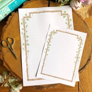 May include: Two blank stationery sheets with a leafy vine border. The border is brown and green with a woodgrain texture. The sheets are lined for writing.