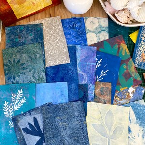 May include: A selection of handmade art prints in shades of blue, teal, and beige. The prints showcase botanical and abstract patterns, including leaf and floral designs. Some prints have a textured appearance, and the overall aesthetic is artistic and handcrafted.