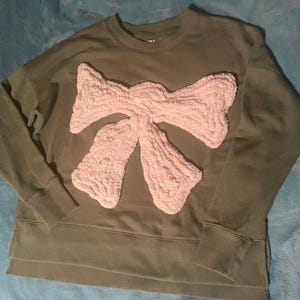 May include: A green sweatshirt with a large pink fluffy bow on the front.