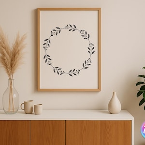 May include: A framed print with a black botanical wreath design hangs above a white cabinet. A clear glass vase with dried pampas grass, two beige mugs, and a white vase are on the cabinet. A potted plant is on the right.