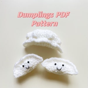 Peut inclure: Trois boulettes blanches en crochet avec des visages souriants. La boulette du haut est fermée, tandis que les deux du bas sont ouvertes. Le texte "Dumplings PDF Pattern" est écrit en rose au-dessus des boulettes.