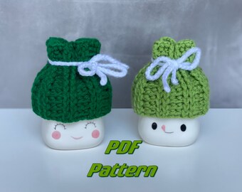 May include: Two white ceramic mugs with green crocheted hats and white yarn bows. The text "PDF Pattern" is written in green below the mugs.