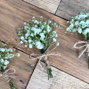 May include: Three small bouquets of white baby's breath flowers tied with twine on a rustic wooden background.