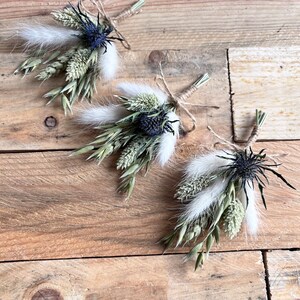 May include: Three small bouquets of dried flowers tied with twine. Each bouquet features dried grasses, white fluffy seed pods, and a dark blue thistle.