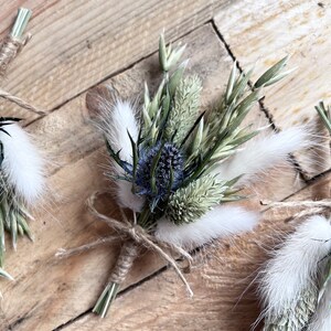 May include: A small bouquet of dried flowers tied with twine. The bouquet includes blue thistle, white bunny tails, and green grasses.