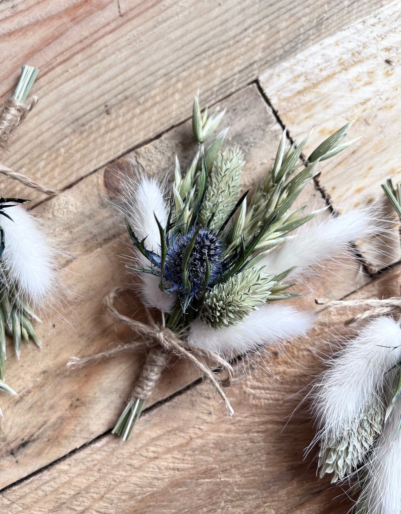 May include: A small bouquet of dried flowers tied with twine. The bouquet includes blue thistle, white bunny tails, and green grasses.