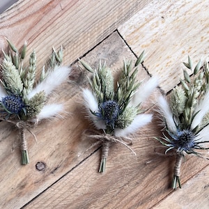 May include: Three small bouquets of dried flowers, each tied with twine. The bouquets feature blue thistle, white bunny tails, and dried grasses.