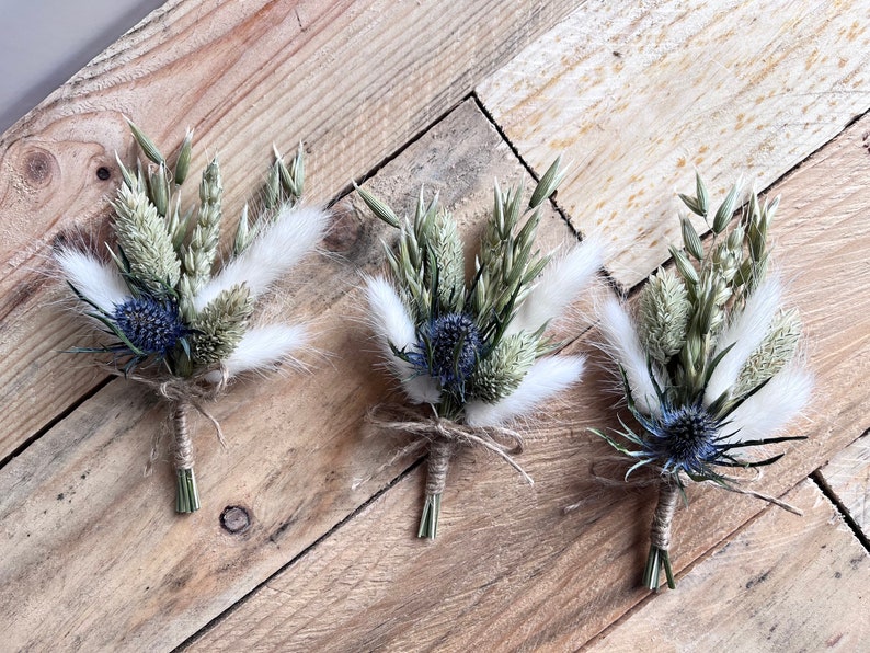 May include: Three small bouquets of dried flowers, each tied with twine. The bouquets feature blue thistle, white bunny tails, and dried grasses.